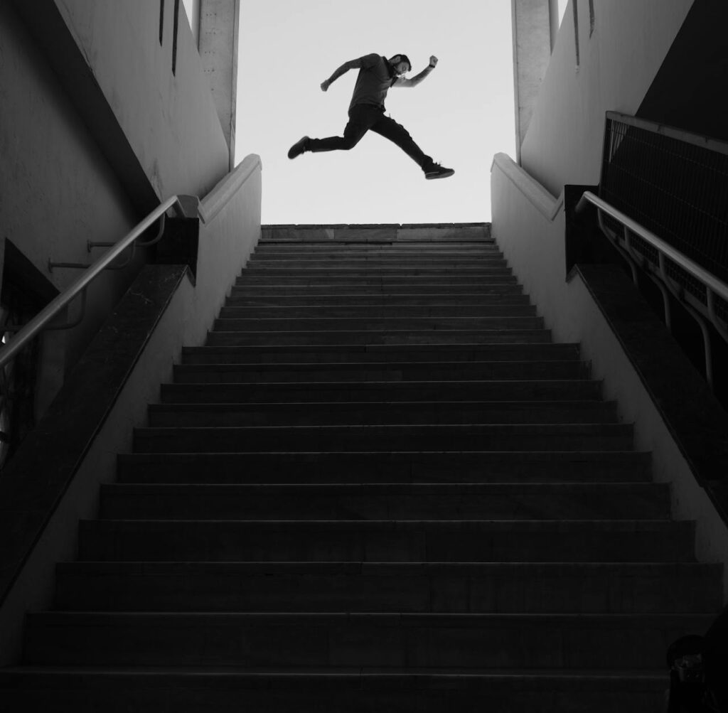 Silhouette of a man performing parkour jump over staircase in minimalistic black and white setting.
