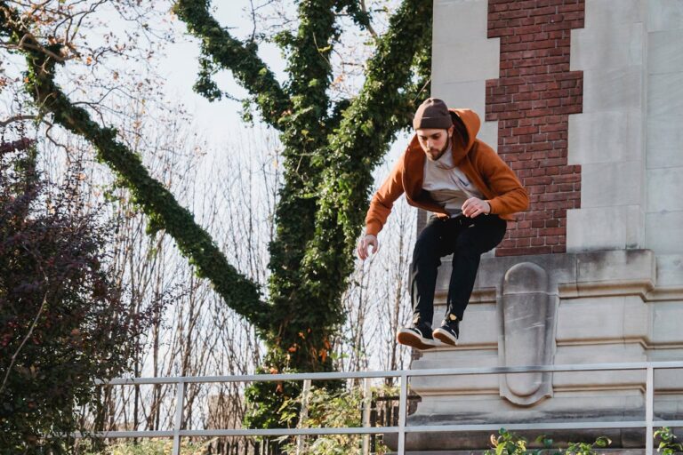 From below full body of brave male athlete doing tricks while practicing parkour in city
