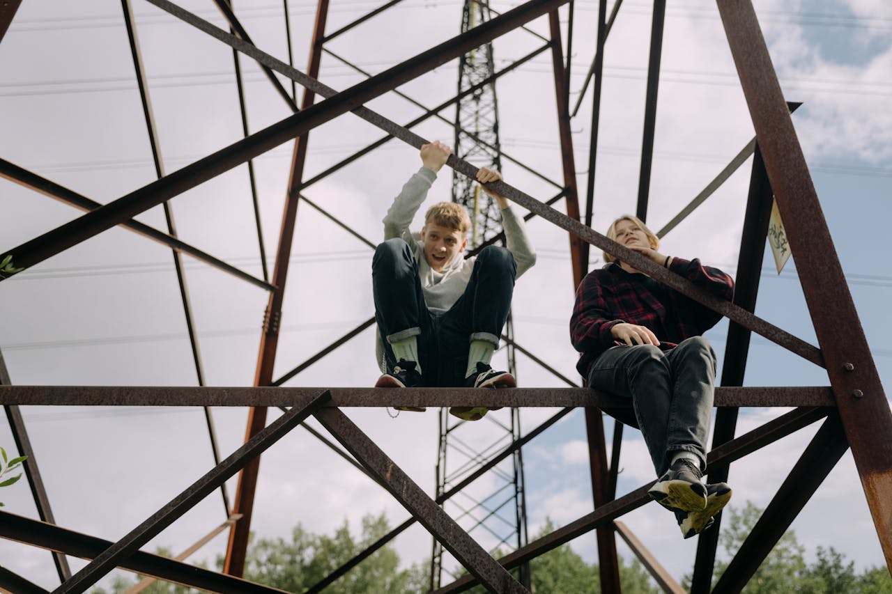Two teenagers sitting and climbing on an electricity pylon with a carefree attitude.