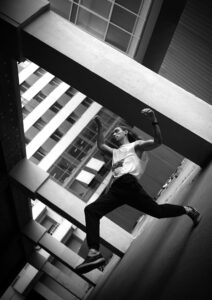 Black and white photo of a parkour athlete performing in an urban setting, showcasing energy and movement.